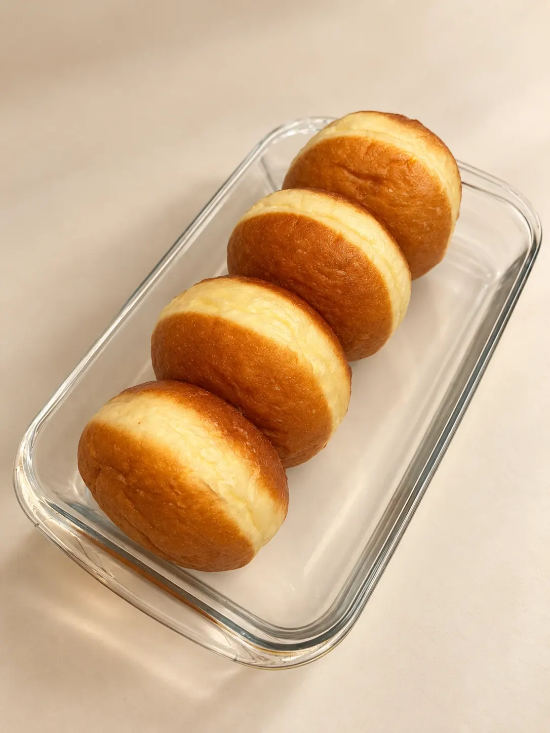 Four golden bomboloni straight from the fryer, before sugar and filling, in a glass dish