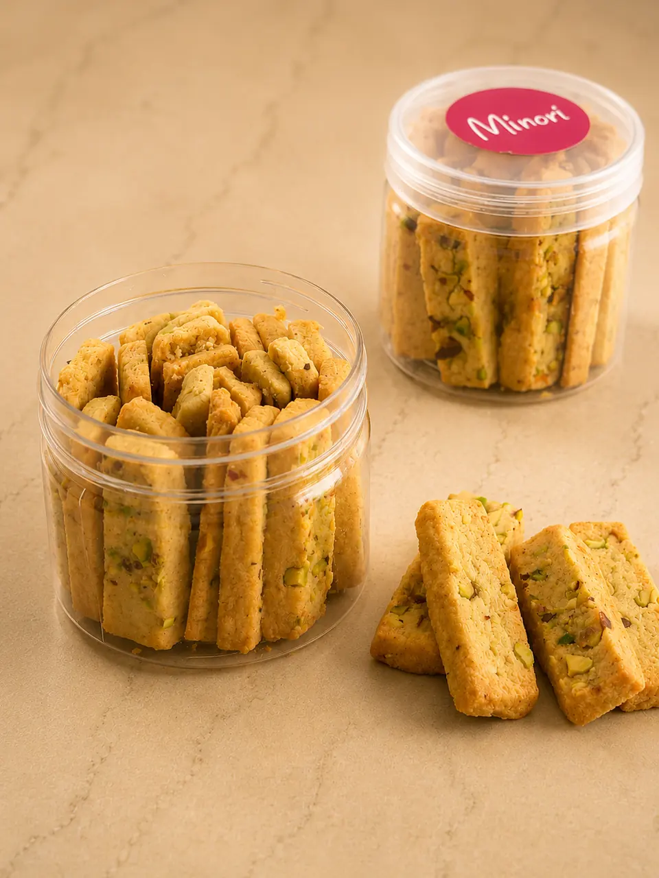 Two Minori jars of twice-baked pistachio biscotti with loose pieces beside them