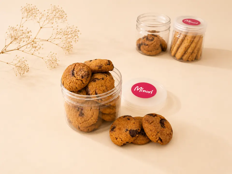 An open Minori jar of choco chip cookies with a biscotti jar behind it